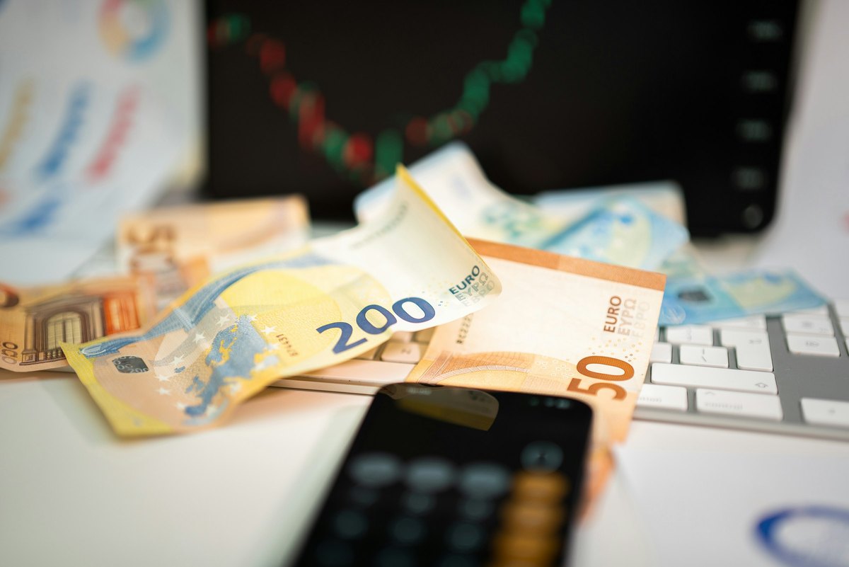 Eurobankbiljetten en een rekenmachine op een bureau voor een scherm met een financiële grafiek